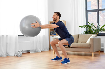 fitness, sport and healthy lifestyle concept - smiling man exercising and doing squats with ball at...