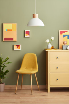 Yellow chair between plant and chest of drawers.