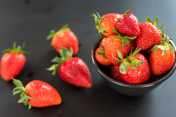 Delicious strawberries in a bowl on black background.