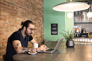 Hipster young man working with his laptop in a coffee shop.