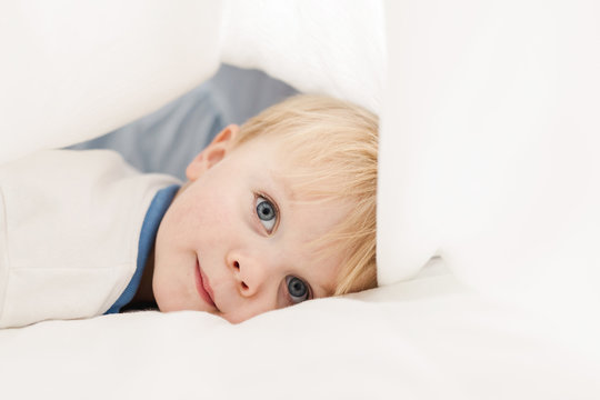 toddler resting under sheets on a bed