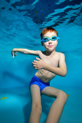 A little boy swims and plays underwater in the pool with his arms apart and looks at the camera....