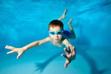 Cute sports boy swimming underwater in the pool. Posing for the camera with glasses. Bottom view...