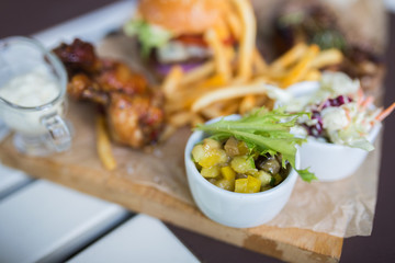 Food plate with fried chicken wings, burger, fried potatoes, sauce, salad, grilled meat . Fast unhealthy tasty food concept