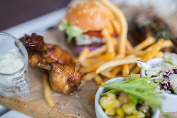 Food plate with fried chicken wings, burger, fried potatoes, sauce, salad, grilled meat . Fast unhealthy tasty food concept