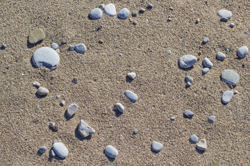 Round flat stones on the beach in the sand, a harsh light. Top view, background