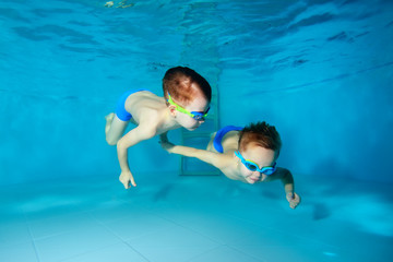 Two beautiful sporty little boys dive to the bottom of the swimming pool, on a blue background. View from the bottom of the pool. Portrait. Underwater photography. Horizontal view