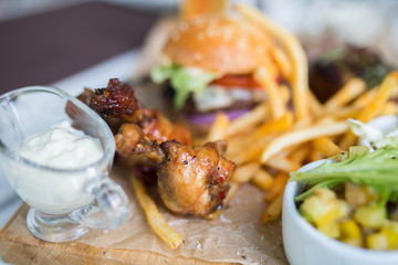 Food plate with fried chicken wings, burger, fried potatoes, sauce, salad, grilled meat . Fast unhealthy tasty food concept