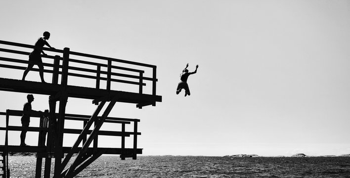 Silhouetted people jumping of a pier in b&w