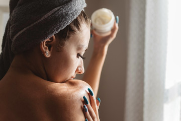 A young woman rubbing lotion on her body after getting out of the shower