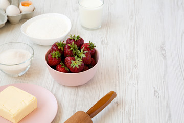 Strawberry pie ingredients (flour, eggs, butter, milk, sugar, strawberry), side view. Cooking strawberry pie or cake. Copy space.
