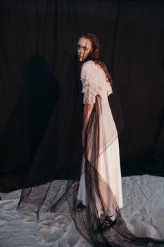 Woman in veil standing near fabric screen in desert