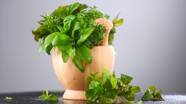 Herbs. Bunch of fresh green organic aromatic herb leaves in wooden mortar with pestle rotated. Mint, Peppermint, Rosemary, Thyme, Sage. Slow motion. 3840X2160 4K UHD video footage