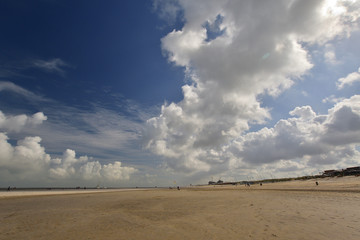 Fototapeta na wymiar Białe pogodne chmury na niebieskim niebie ponad nadmorską plażą.