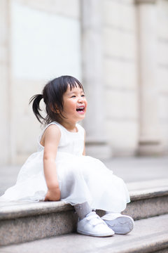 Smiling little girl in white dress sitting outdoors