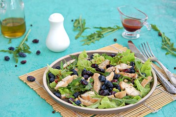 Light salad with arugula, lettuce, grilled chicken and honeysuckle on a brown plate on a turquoise background. Healthy food, diet. Selective focus
