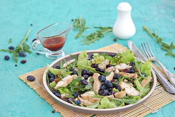 Light salad with arugula, lettuce, grilled chicken and honeysuckle on a brown plate on a turquoise background. Healthy food, diet. Selective focus