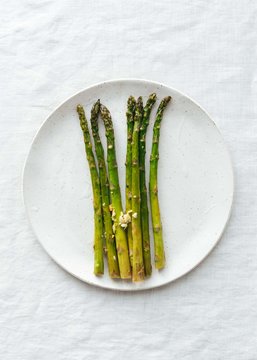 Roasted asparagus, lemon, garlic on ceramic plate and linen tablecloth