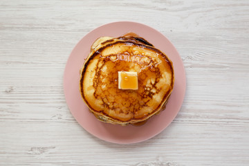 Homemade pancakes with butter and maple syrup on a pink plate, overhead view. Top view, flat lay, from above. Close-up.