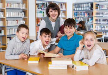 Smiling pupils with teacher sitting in school library