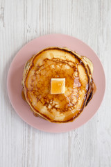 Homemade pancakes with butter and maple syrup on a pink plate over white wooden background, overhead view. Top view, flat lay, from above.