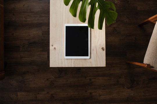 white tablet on modern plywood table with decorative green leaf