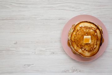 Homemade pancakes with butter and maple syrup on a pink plate, view from above. Overhead, flat lay, top view. Copy space.