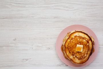 Homemade pancakes with butter and maple syrup on a pink plate, top view. Overhead, flat lay, from above. Copy space.