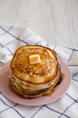 Homemade pancakes with butter and maple syrup on a pink plate, low angle view. Copy space.