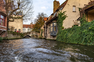 Fototapeta na wymiar Picturesque old street of Bruges with traditional medieval houses, ivy, canal and bridges. Cityscape of Bruges streets shot from the boat.