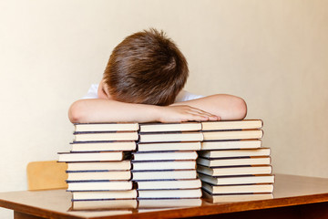 the child sits at the table, putting his head on the books.