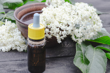 Obraz na płótnie Canvas Elderberry essential oil or extract of tincture with elderberry flowers on a wooden background.