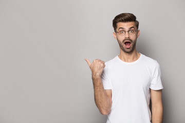 Amazed funny guy in glasses pointing finger aside at copyspace