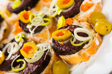 Tasty canapes with blood sausage, bread, olives and onion  at plate