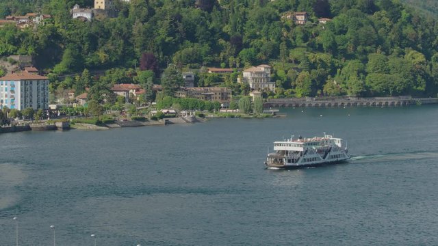Aerial shot of a ferry for tourists in lago maggiore with the town of Stresa Verbania behind on a sunny day.