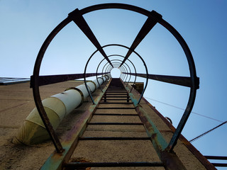 Looking up a industry fire ladder leading into the blue sky - concentric view