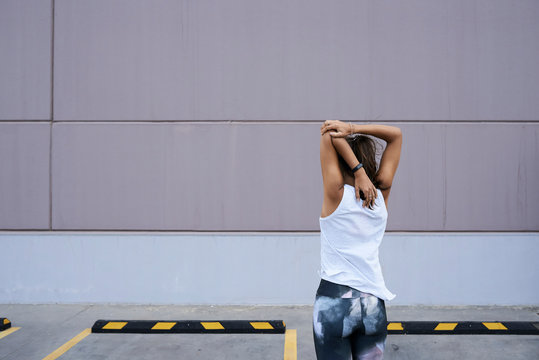 Sportswoman stretching arms against wall.
