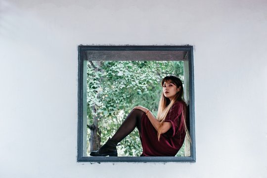Attractive young female with long hair sitting in square window