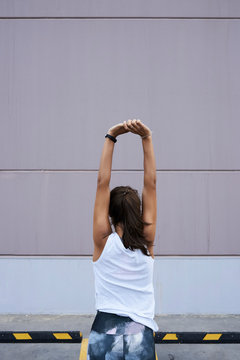Minimal view of sportswoman stretching arms against wall.
