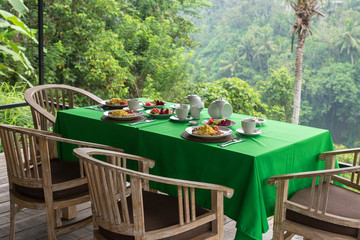 Table with served breakfast on terrace with jungle view in Bali