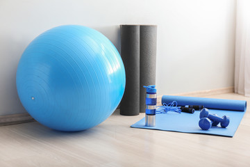 Set of sports equipment with fitness ball and bottle of water near light wall - obrazy, fototapety, plakaty