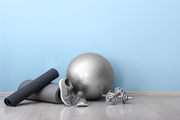 Set of sports equipment with fitness ball and shoes near color wall