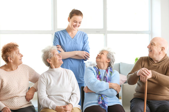 Young caregiver with group of senior people in nursing home