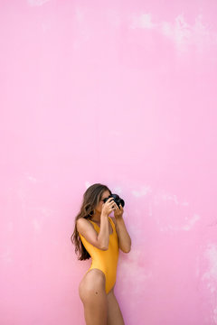 minimalistic photo, a girl in a yellow swimsuit is standing and taking pictures on the camera. pink background
