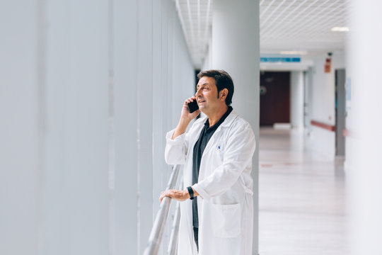 Doctor talking on cellphone while looking through the window. He is calm and relax.