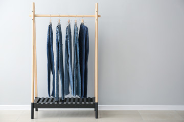 Clothes rack with stylish jeans pants near light wall