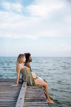 Multicultural couple sitting on wooden dock over the mediterranean sea