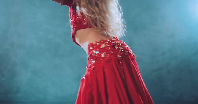 Oriental movement waist and hips. Blond girl twists her skirt and hair. Back view.