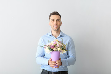Handsome man with bouquet of beautiful flowers on light background