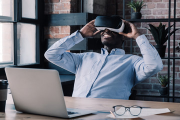 Young African male wearing virtual eality headset and holding it willing to see more and enjoy...